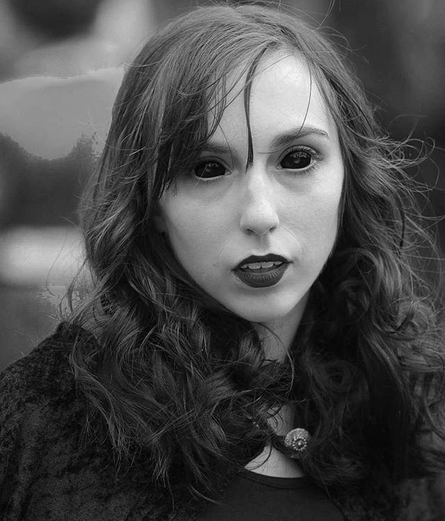 A black and white portrait of a young woman with striking black eyes and dark lipstick, creating a mysterious and intense mood.