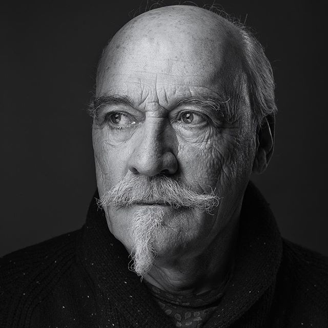 A black and white portrait of a distinguished senior man with a unique mustache and beard looking thoughtfully to the side.