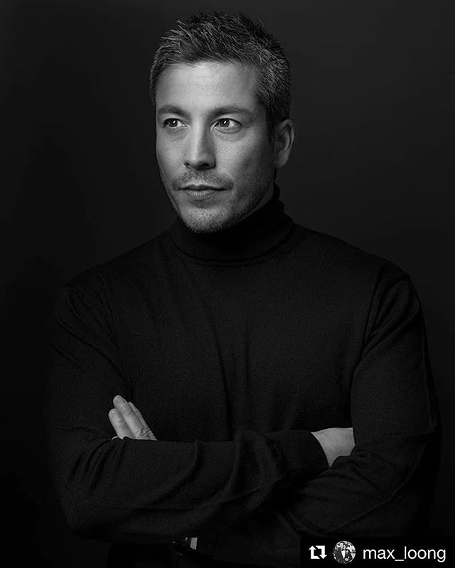 A black and white portrait of a man with a turtleneck and his arms crossed against a dark background.