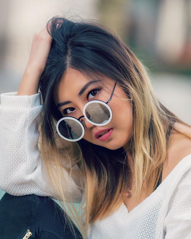 Portrait of a fashionable young woman with round sunglasses, looking dreamy and relaxed in soft outdoor light.