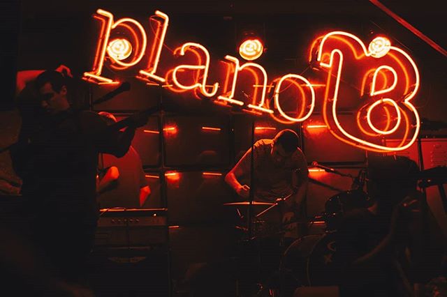 A band plays live on stage under a glowing neon sign in a dimly lit music venue.