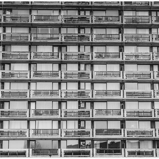 Architectural facade of a modern building with rows of windows and balconies in a grayscale format, evoking a sense of urban design.