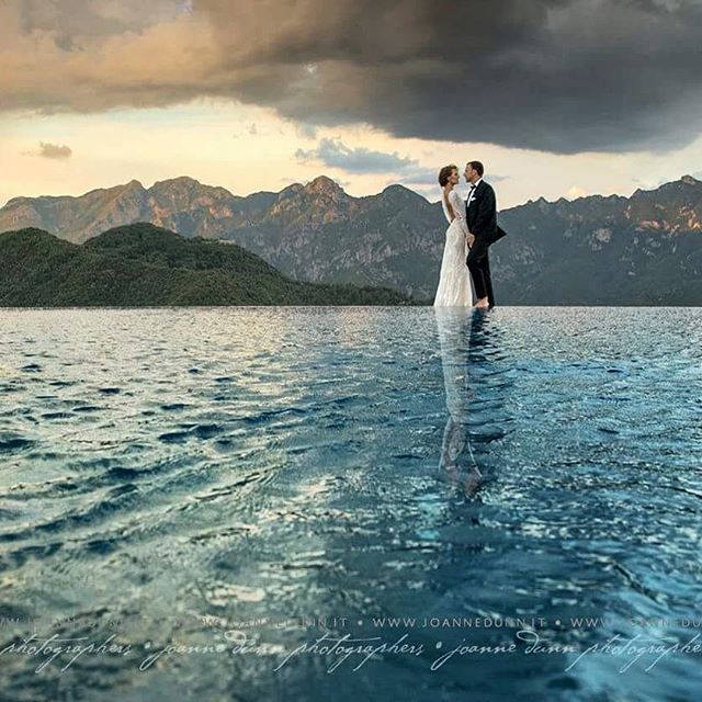 A bride and groom embrace tenderly on a lake, with mountains in the background, creating a romantic wedding moment.