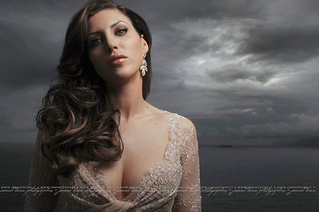 Elegant woman in dress poses against a dramatic stormy sky and ocean backdrop.