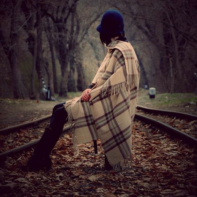 A woman sits on a railway track wrapped in a scarf, set in an autumn forest.