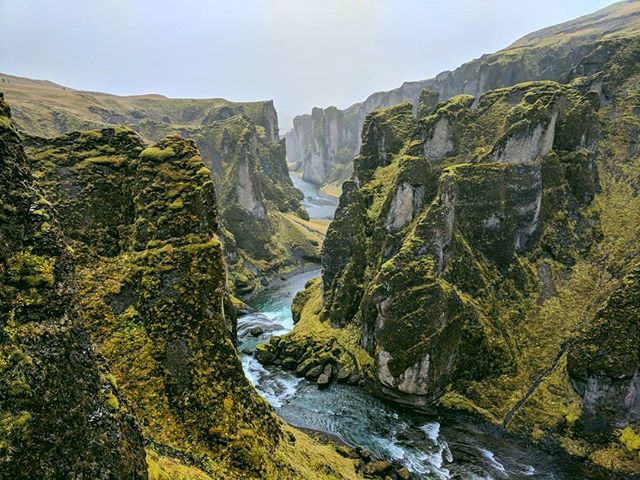 A scenic view of Fjadrargljufur canyon in Iceland, with a river flowing through its mossy cliffs.