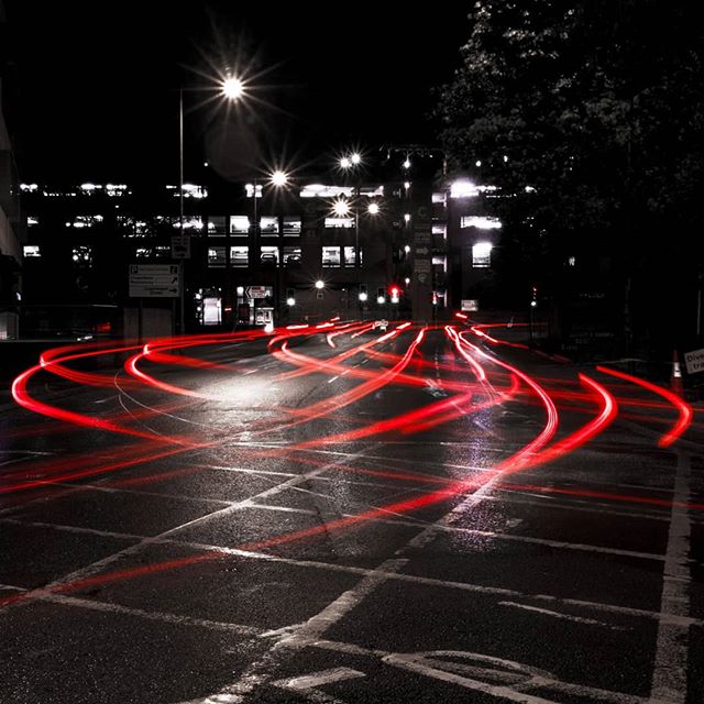 Abstract image of red light trails curving on a city street at night with buildings and street lights.