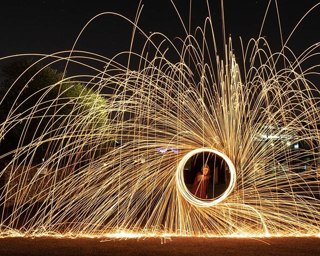 A person is captured in a stunning light painting with swirling sparks at night using steel wool.