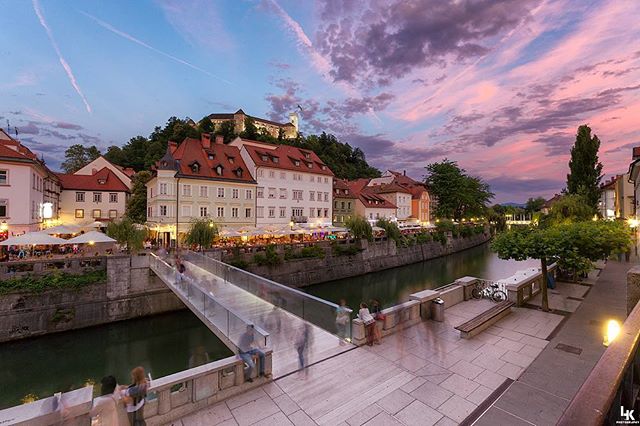 Picturesque cityscape view of Ljubljana, Slovenia with a bridge over the river and buildings under a colorful sky.