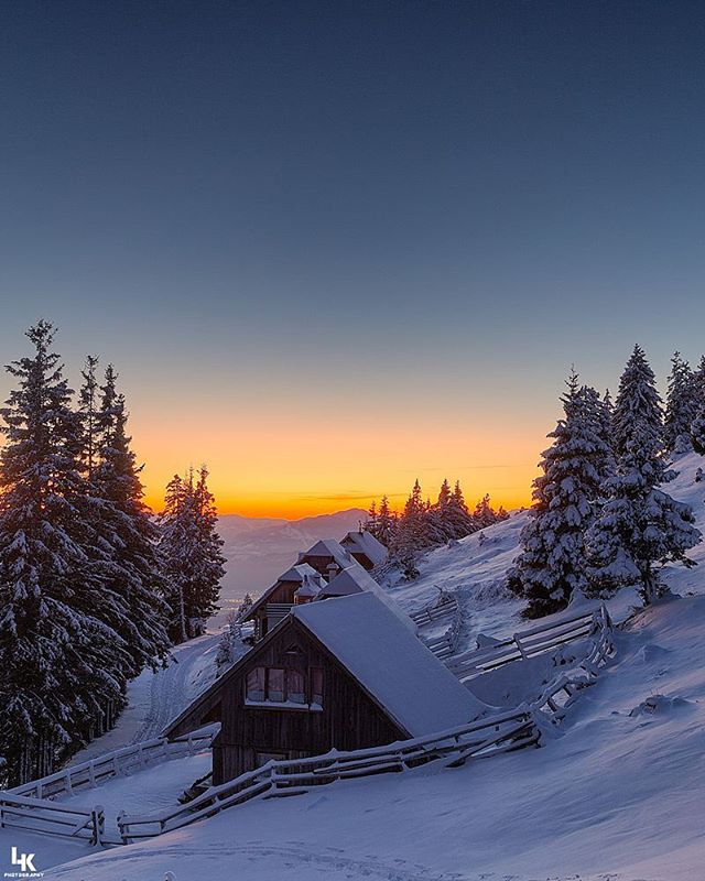 Snowy mountain scene with cabins during sunset. The sun sets behind distant peaks.