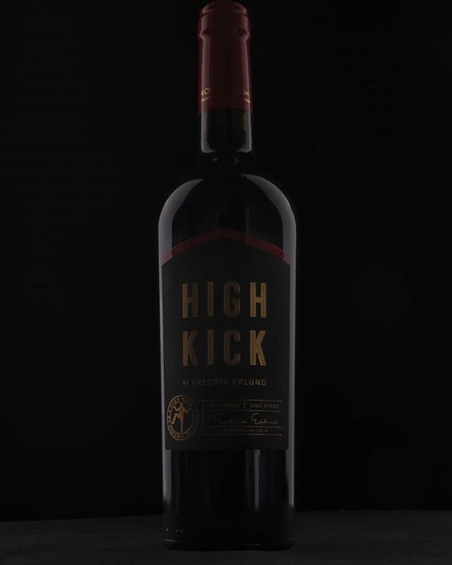 A bottle of High Kick red wine stands against a dark backdrop, showcasing its sleek and modern design.