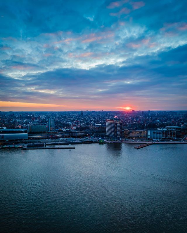 Aerial view of Amsterdam cityscape at sunset with a calm river, buildings and a colorful sky.