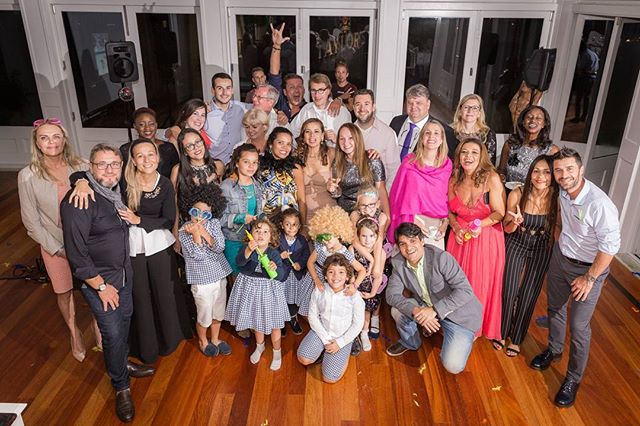 A large group of happy adults and children pose for a photo at an indoor party.