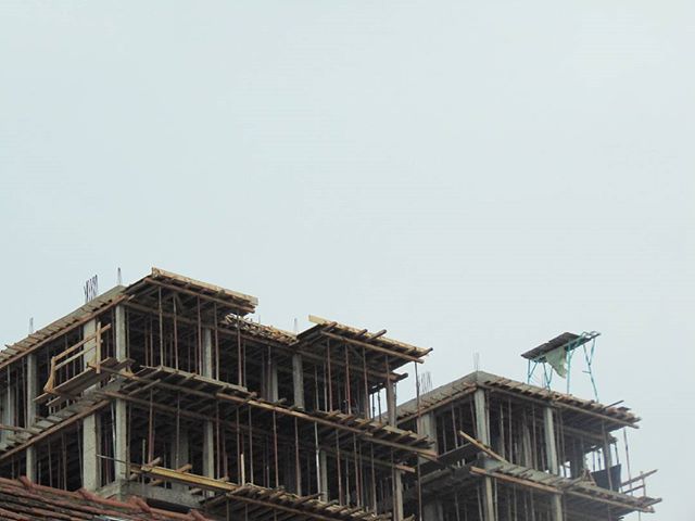 Unfinished building under construction with scaffolding against a cloudy sky, showcasing urban development.