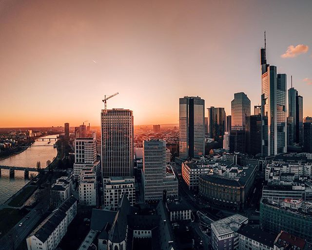 Aerial view of the Frankfurt skyline at sunset with the Main River in the foreground.