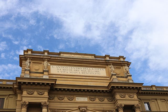 Architectural detail of a historic building with statues, text, and blue sky. 