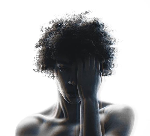 A person with curly hair poses in a moody, artistic portrait against a white background.