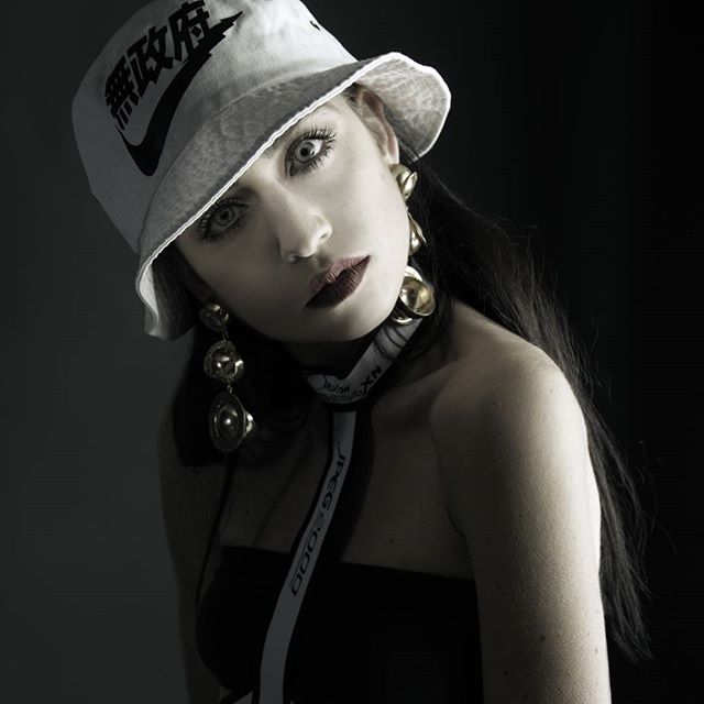 Stylish woman in bucket hat and gold earrings against a dark background. Editorial style.
