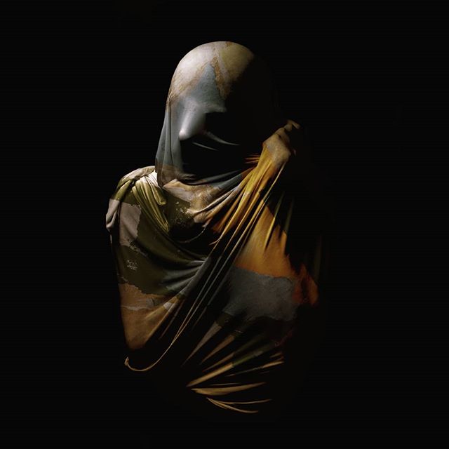Artistic draped figure shrouded in earth-toned fabric against a dark background, evoking a sense of mystery and elegance.