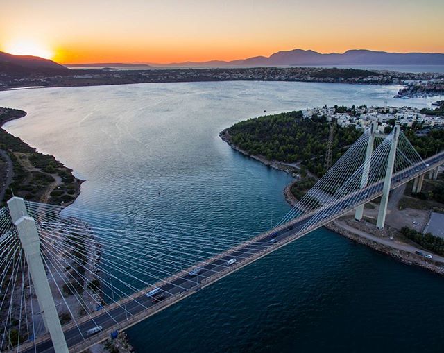 A scenic view of a bridge spanning a waterway at sunset, with mountains visible in the distance.