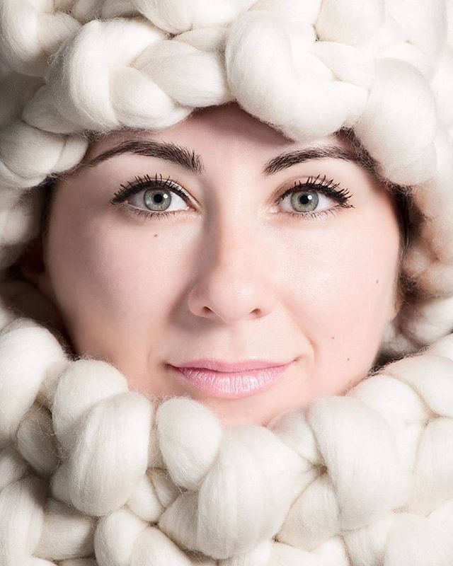 A woman's face is framed by soft white wool in a serene, close-up portrait.