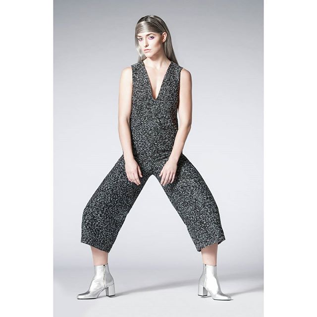A woman poses in a gray jumpsuit and silver boots against a white background.