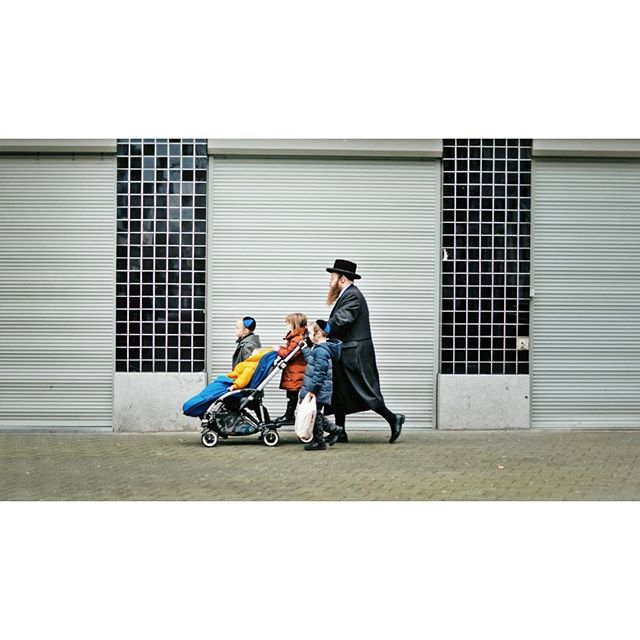 A man walks with his children, one in a stroller, in an urban setting.