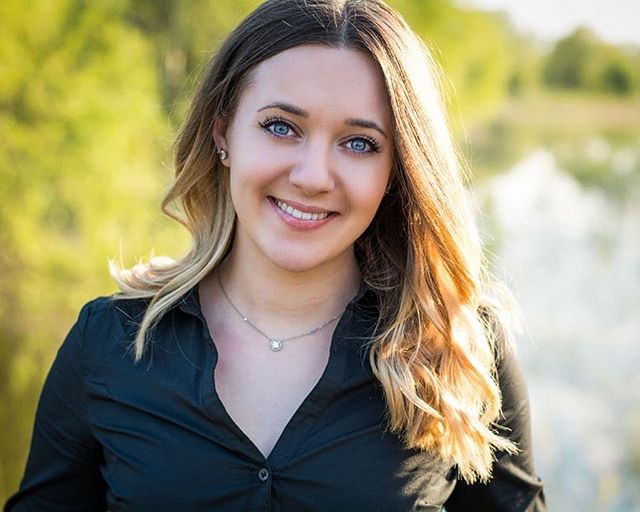 A smiling woman with blue eyes poses for a portrait outdoors in soft, natural light.