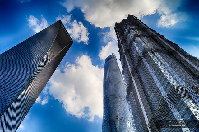 A low angle shot of modern skyscrapers reaching into a vibrant blue sky with fluffy white clouds in an urban landscape.