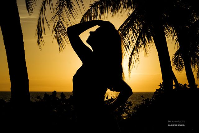 A silhouette of a woman at sunset with palm trees in a tropical setting.