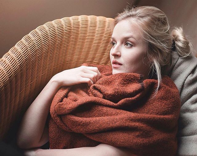 Woman wrapped in a blanket relaxing on a wicker couch, looking peaceful and serene indoors.