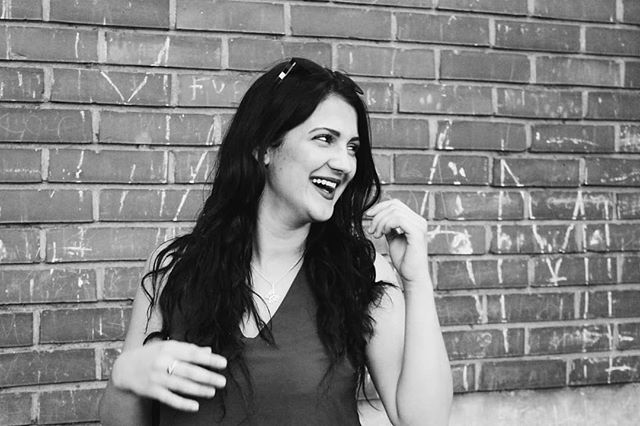 A brunette woman laughs in front of a brick wall in this black and white outdoor shot.