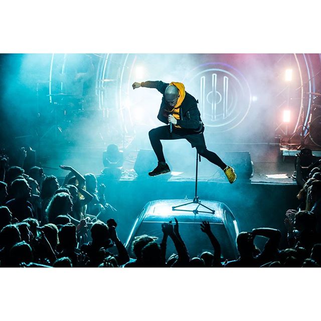 A man performs on stage with a microphone in front of a large crowd at a concert.