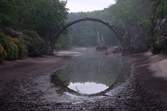 Rakotz Bridge, reflected in still water, creates a perfect circle in a misty, scenic landscape in Kromlau, Germany.