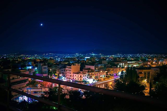 Night cityscape with city lights illuminating buildings under a crescent moon.