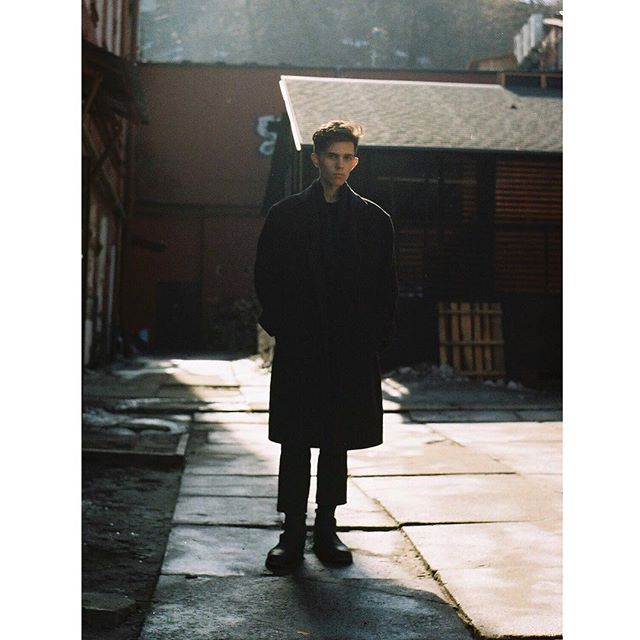 A stylish man in a coat stands in an urban alleyway, embodying city life and minimalist fashion.