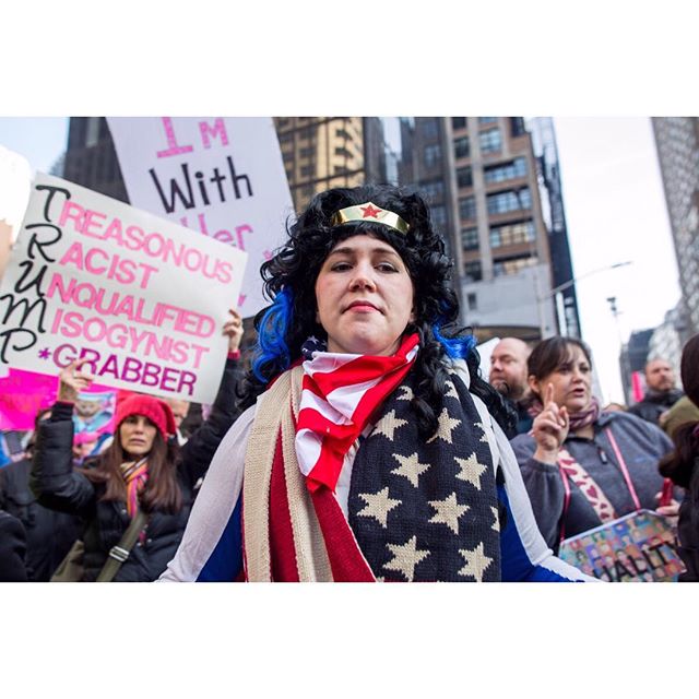 A woman dressed as Wonder Woman protests with a sign at a rally. 