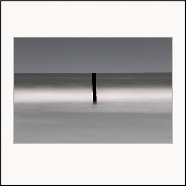 A minimalist seascape featuring a dark pole in a calm ocean with a tranquil, monochrome aesthetic.