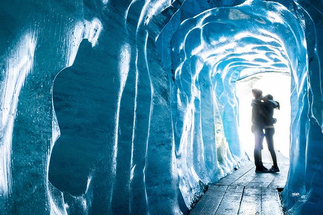 A couple kisses in a naturally formed blue ice cave with soft backlighting, creating a romantic and intimate moment.