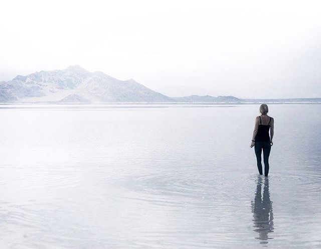 A woman stands in a calm lake with mountains in the distance, creating a serene, natural scene.
