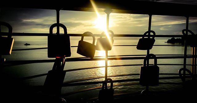 Locks attached to railings capture a waterfront sunset in a romantic travel destination.