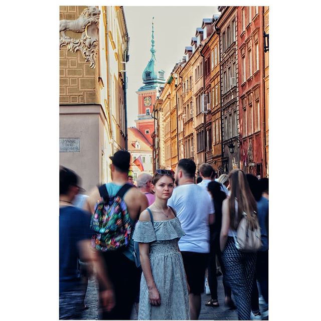 A woman stands on a crowded city street surrounded by buildings in an old European town.