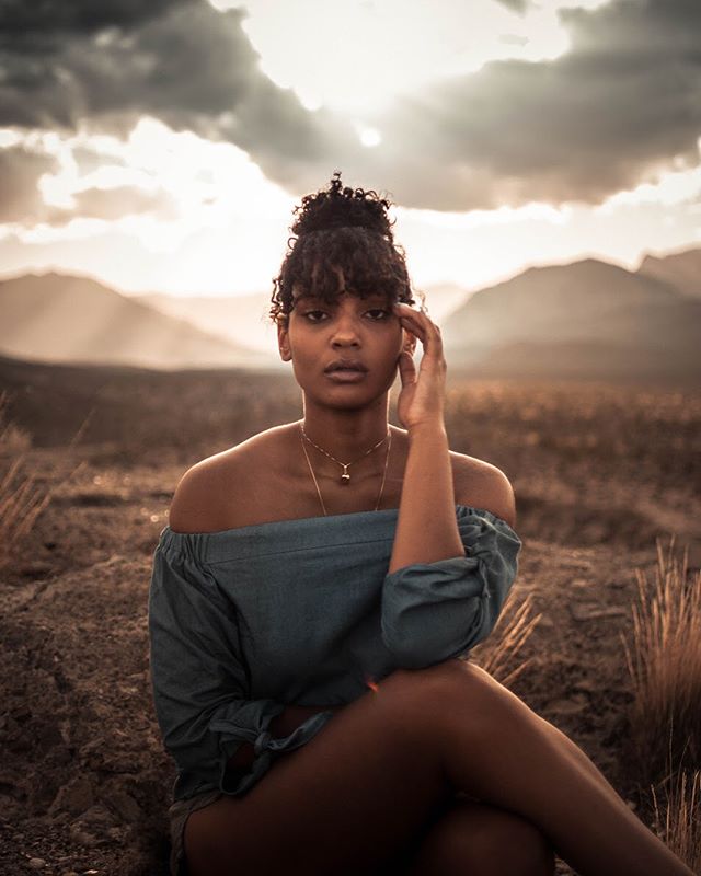 A woman poses in a field with mountains in the background.