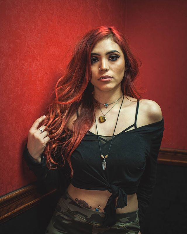 A confident redhead poses in a studio setting, showcasing a trendy fashion and beauty look.