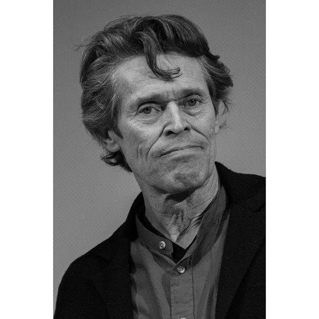 A black and white portrait of actor Willem Dafoe, showcasing his intense and serious demeanor.