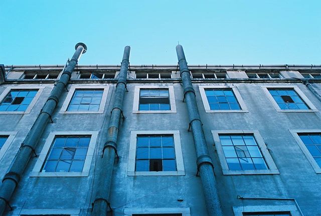 An aged building facade with pipes against a blue sky, conveying urban architecture and industrial design.