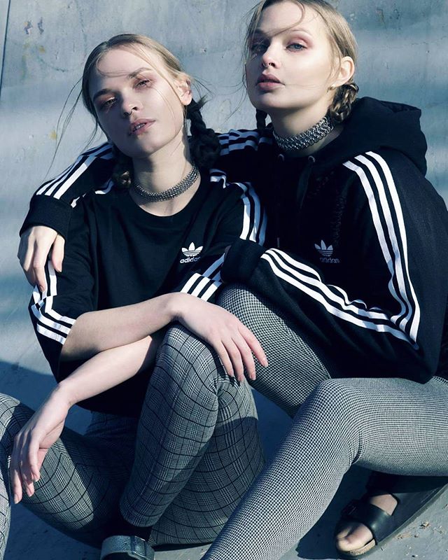 Two women wearing Adidas clothing and chokers pose outdoors in a stylish editorial shot.