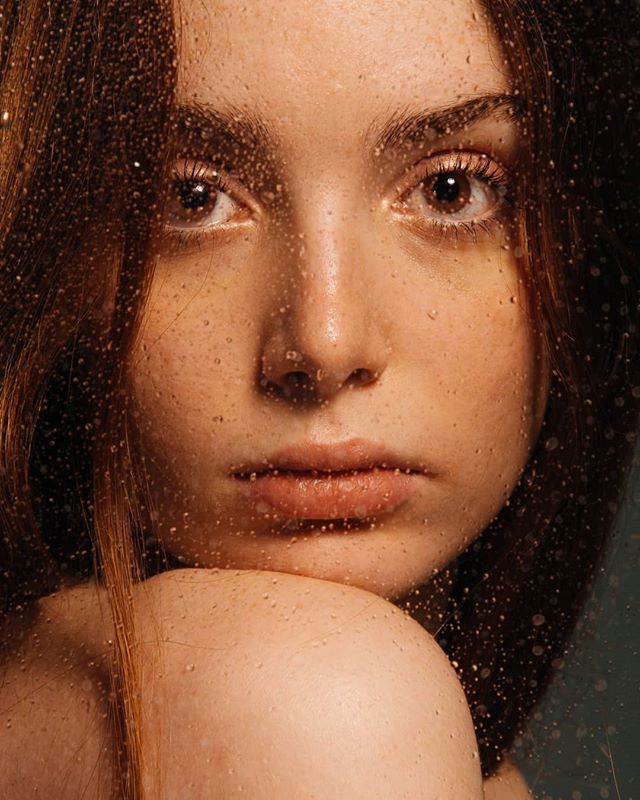 Close-up portrait of a woman's face with water droplets, showcasing a soft and sensual mood.
