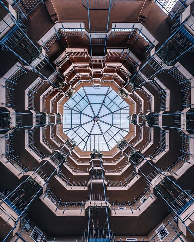 A low-angle shot showcases a multi-story building's interior with balconies and geometric architecture, viewed through a glass roof.