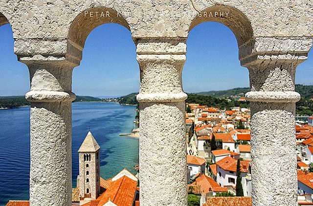 Scenic view of Rab, Croatia, featuring architecture and coastal landscape through stone arches.